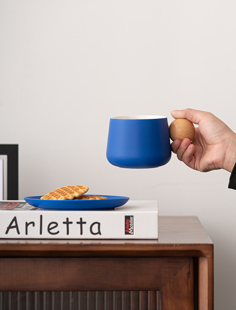 Hand holding blue ceramic coffee cup with wood handle