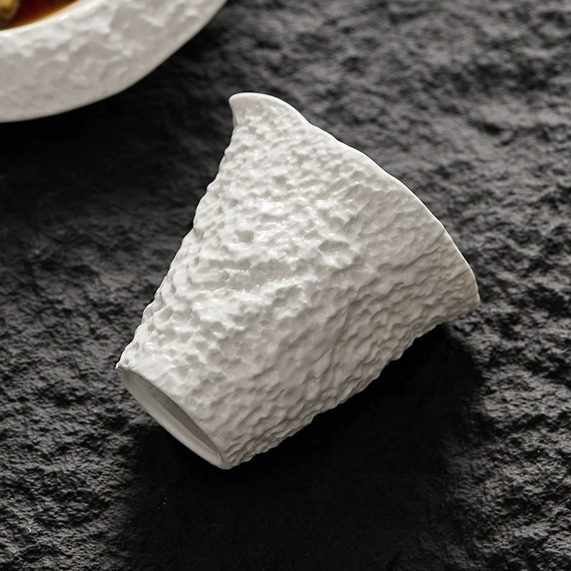 Hand holding rock-pattern ceramic pitcher over seafood dish