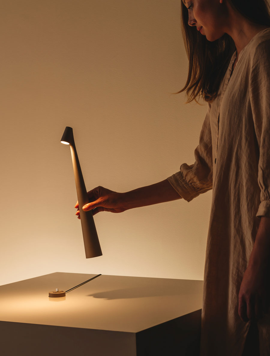 Person holding a modern lamp with a warm glow in a minimalistic setting
