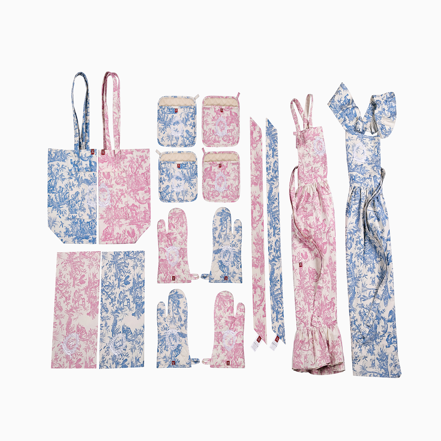 A comprehensive flat lay of the 11-piece Toile de Jouy collection in pink, featuring the apron, tote, napkins, and oven mitts.