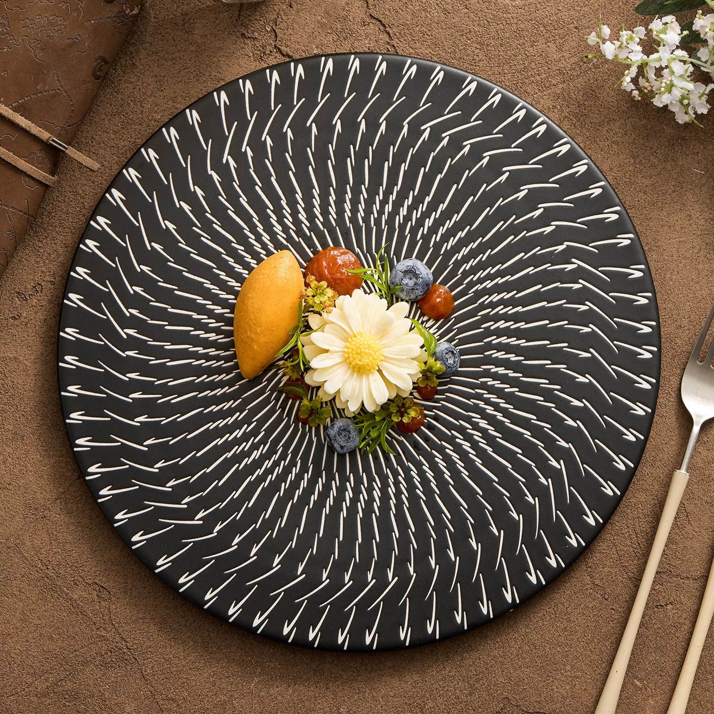 Decorative black plate with white patterns featuring a floral arrangement on a brown surface.