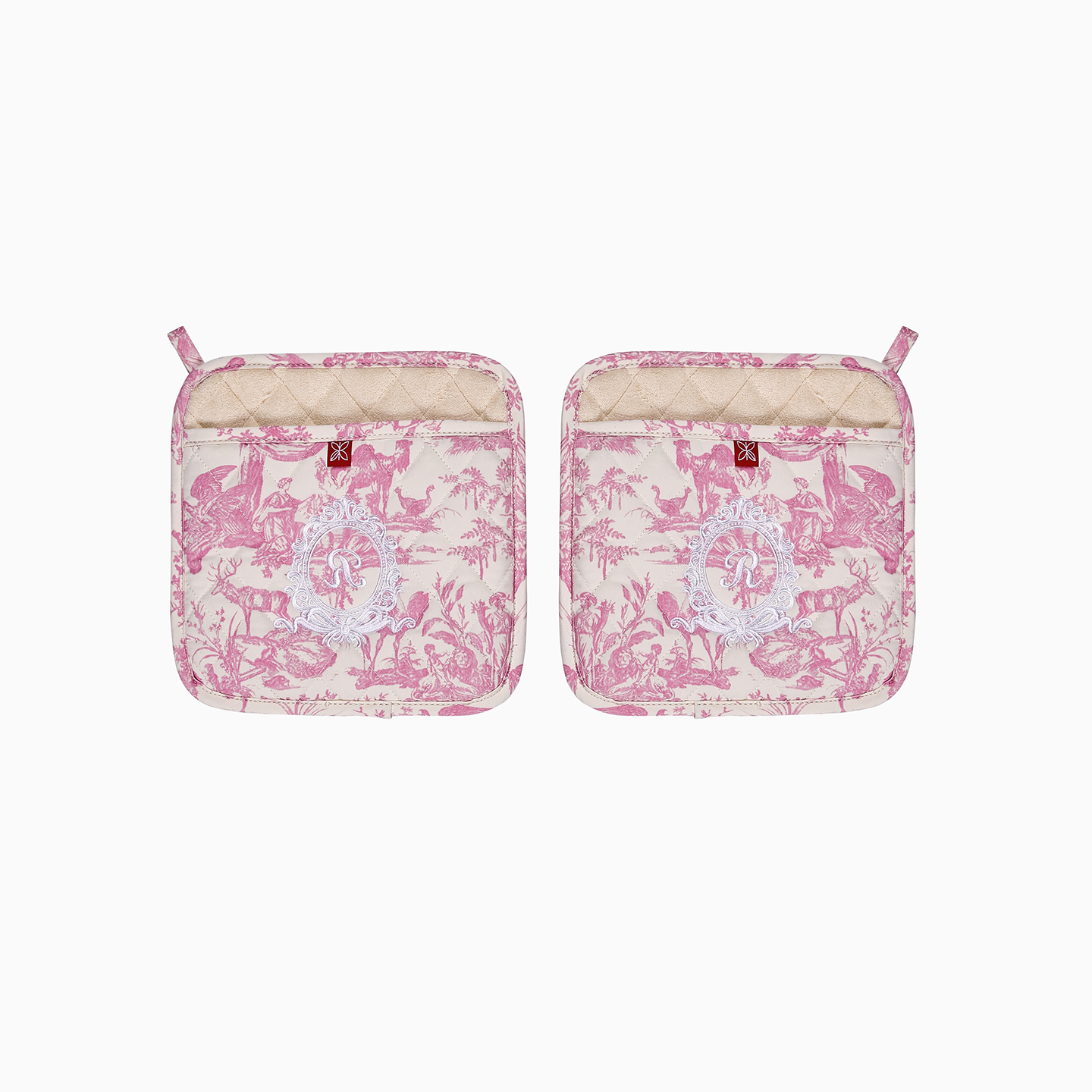 A square pink French Toile de Jouy pot holder featuring a white royal-inspired embroidered emblem and hanging loop.