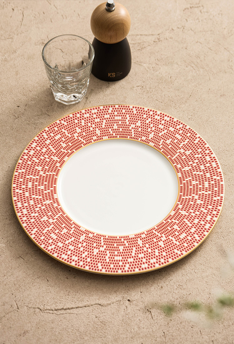 Artistic food presentation with fresh herbs and reduction sauce on a red patterned plate.