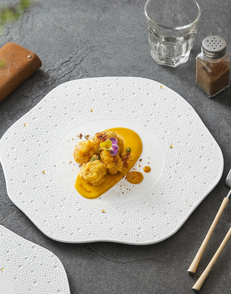 Artistic white porcelain dinner plate featuring irregular wave edges and delicate gold speckles for a refined modern dining aesthetic