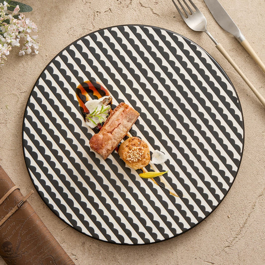 Round black and white patterned plate with a dish of food on a beige surface.