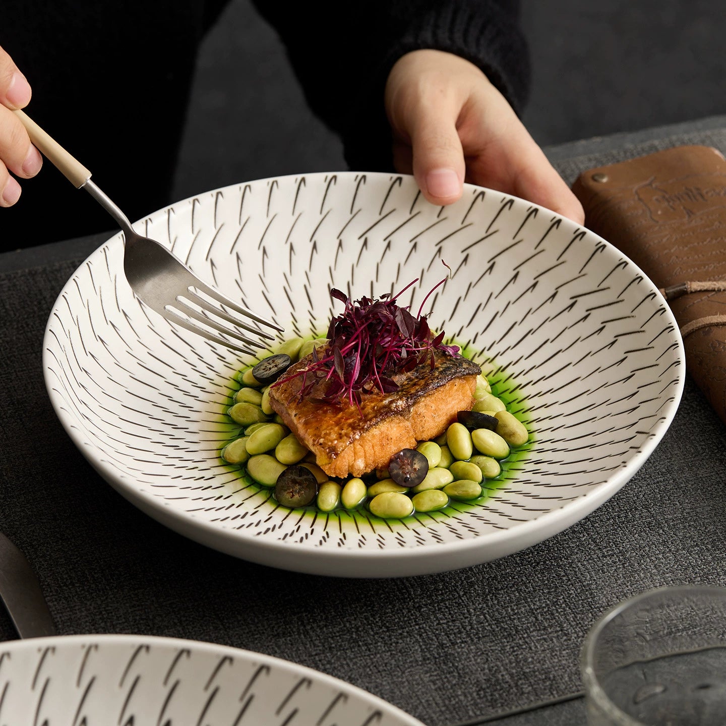 Dish with salmon and vegetables on a textured plate, held by a person.