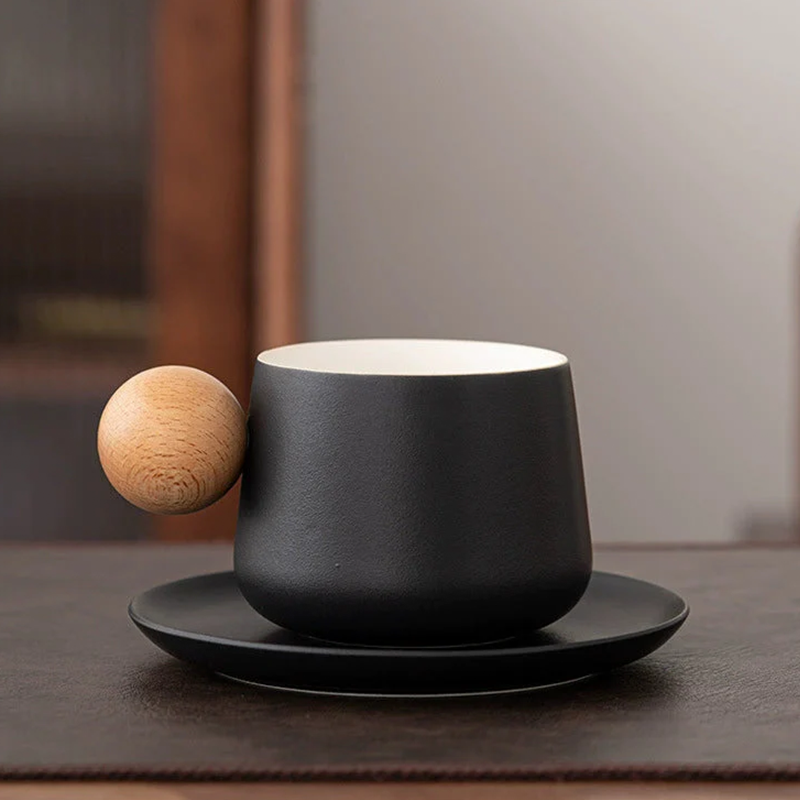 Black cup and saucer with a wooden ball on a textured surface