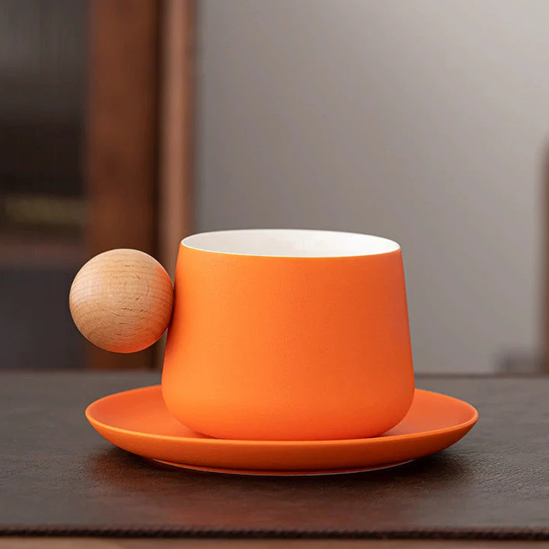 Orange cup and saucer with a wooden ball on a dark surface