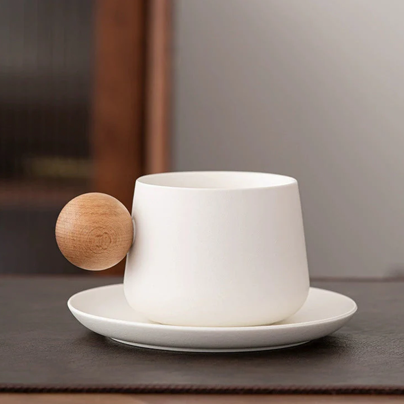 White ceramic cup and saucer with a wooden ball on a gray surface