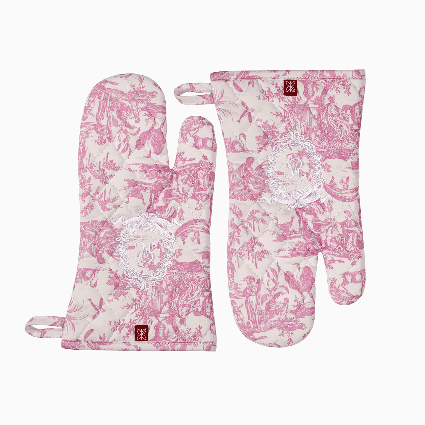 Close-up of a pink Toile de Jouy oven mitt featuring an intricate white embroidered royal emblem.
