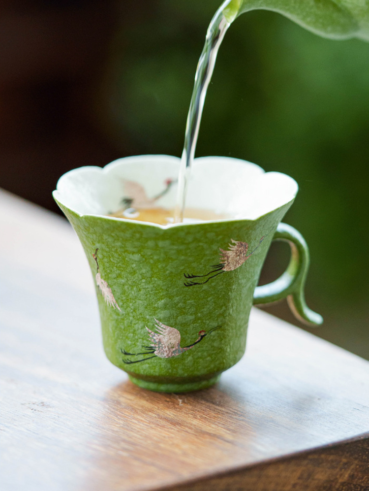 Close-up of celadon glaze porcelain teacup with silver crane details