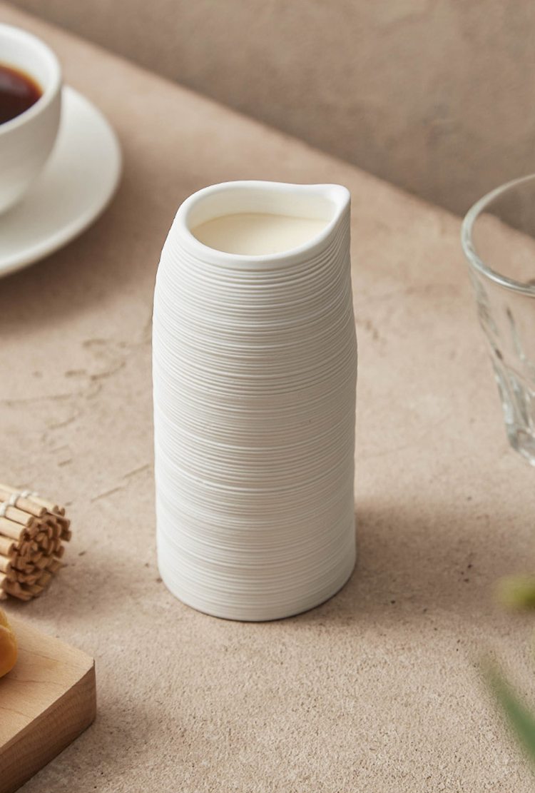 White ceramic pitcher on a beige surface with a cup and glass in the background