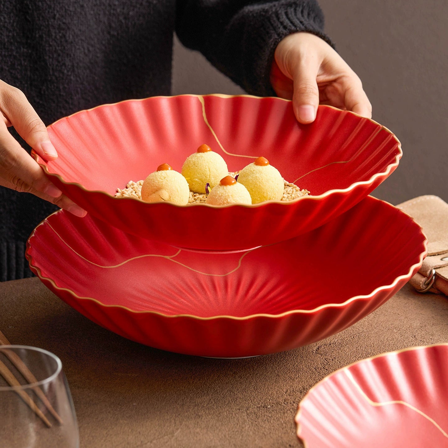 Red decorative bowl with scalloped edges holding small desserts on a brown surface.