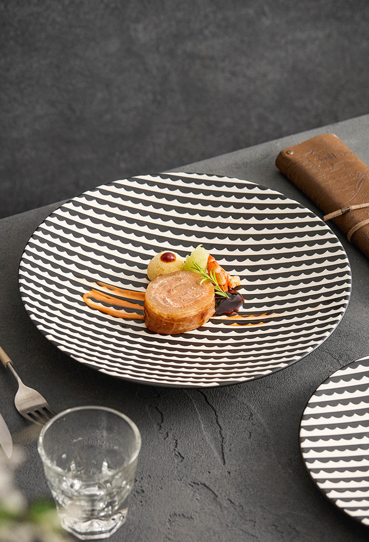 Black and white patterned plate with a small dish of food on a dark surface.