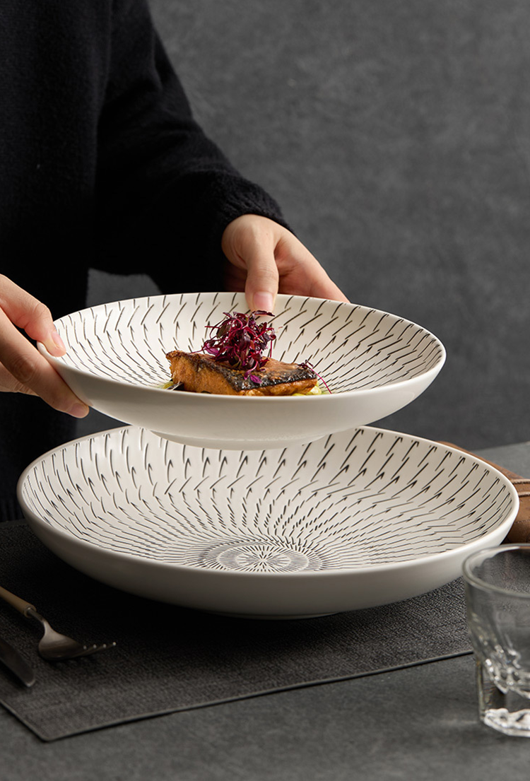 Person holding a white bowl with decorative patterns, containing food, on a dark surface.