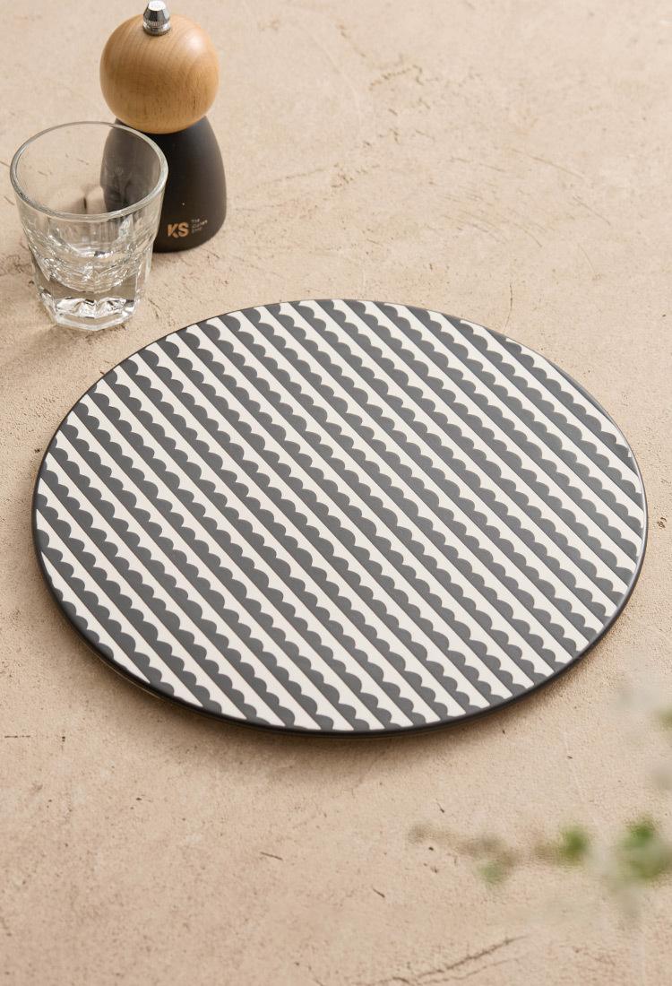 Round gray and white patterned placemat on a beige surface with a glass and pepper grinder.