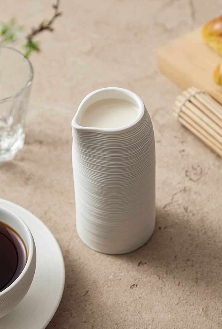White ceramic pitcher on a textured surface with a glass and cup in the background