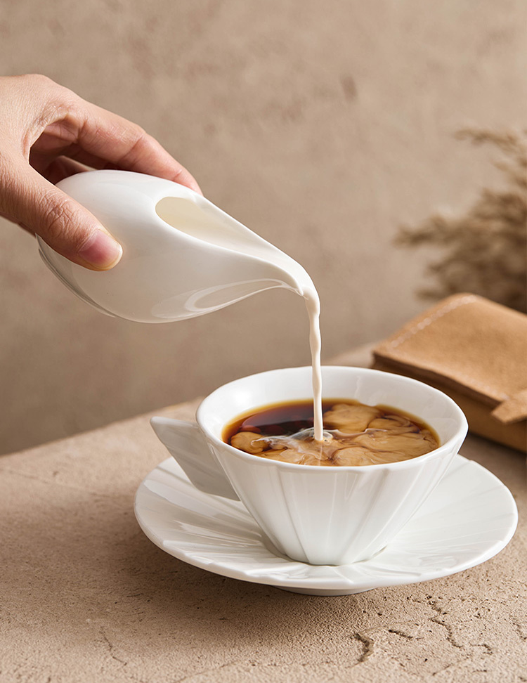 Ergonomic palm-grip ceramic sauce pitcher being held for a clean pour.