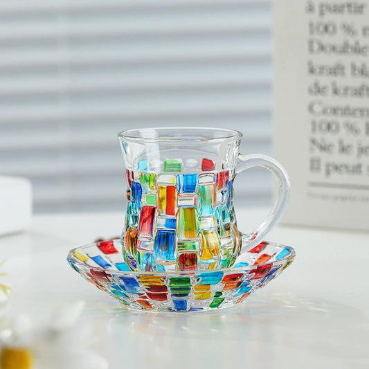 Hand-painted retro glass cup with handle and matching saucer on wooden table

