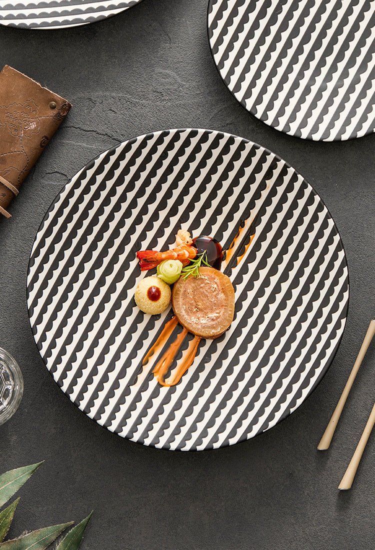 Round black and white patterned plate with a dish of food on a dark surface.