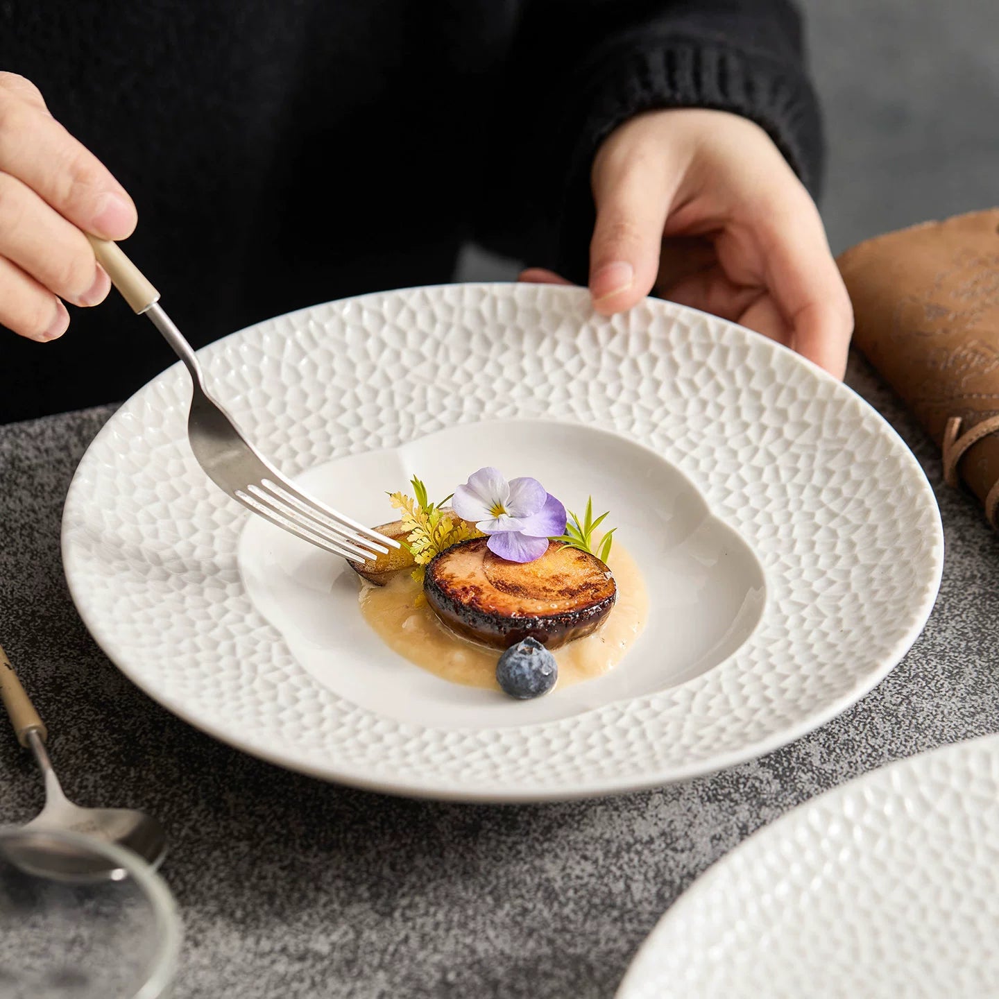 High-contrast plating of seared protein and edible flowers on a blossom-well dish.