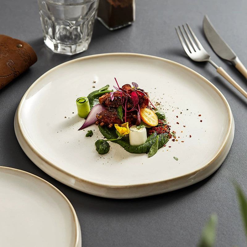 Delicate dish of vegetables on a white plate with cutlery and glasses in the background.