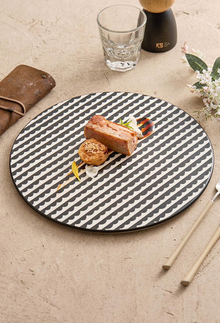 Round black and white patterned plate with a dish on a beige surface