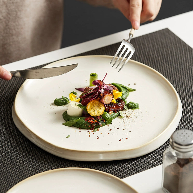 Person about to eat a gourmet salad on a white plate with a fork and knife.