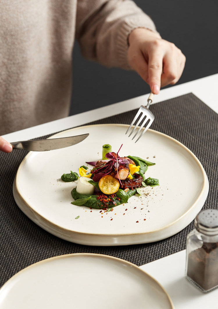 Person about to eat a dish of salad with a fork and knife on a white plate.