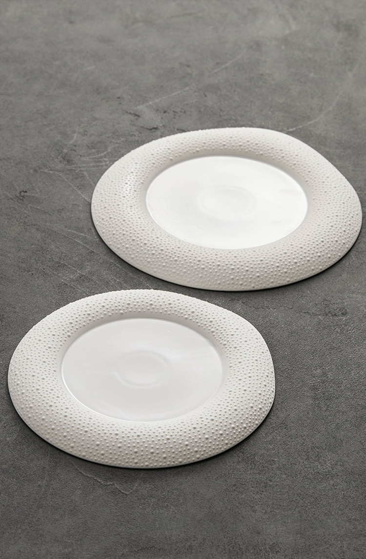 Matte white ceramic plate with raised rim pattern under natural lighting.