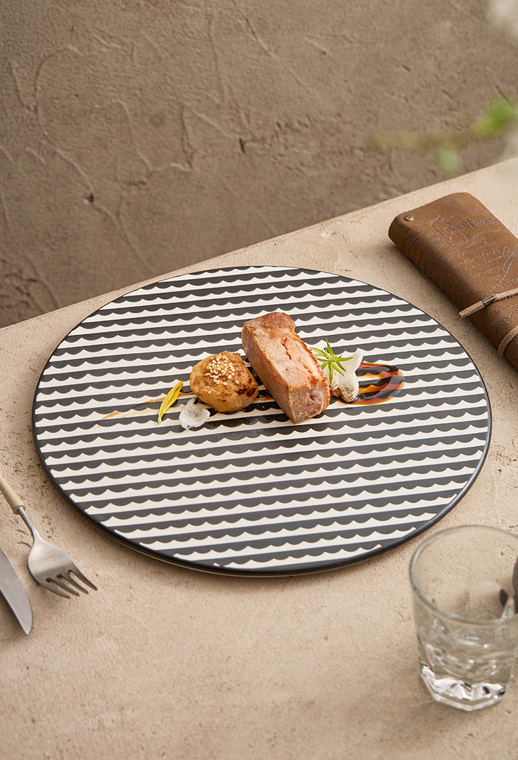 Round black and white patterned plate with a dish on a textured surface