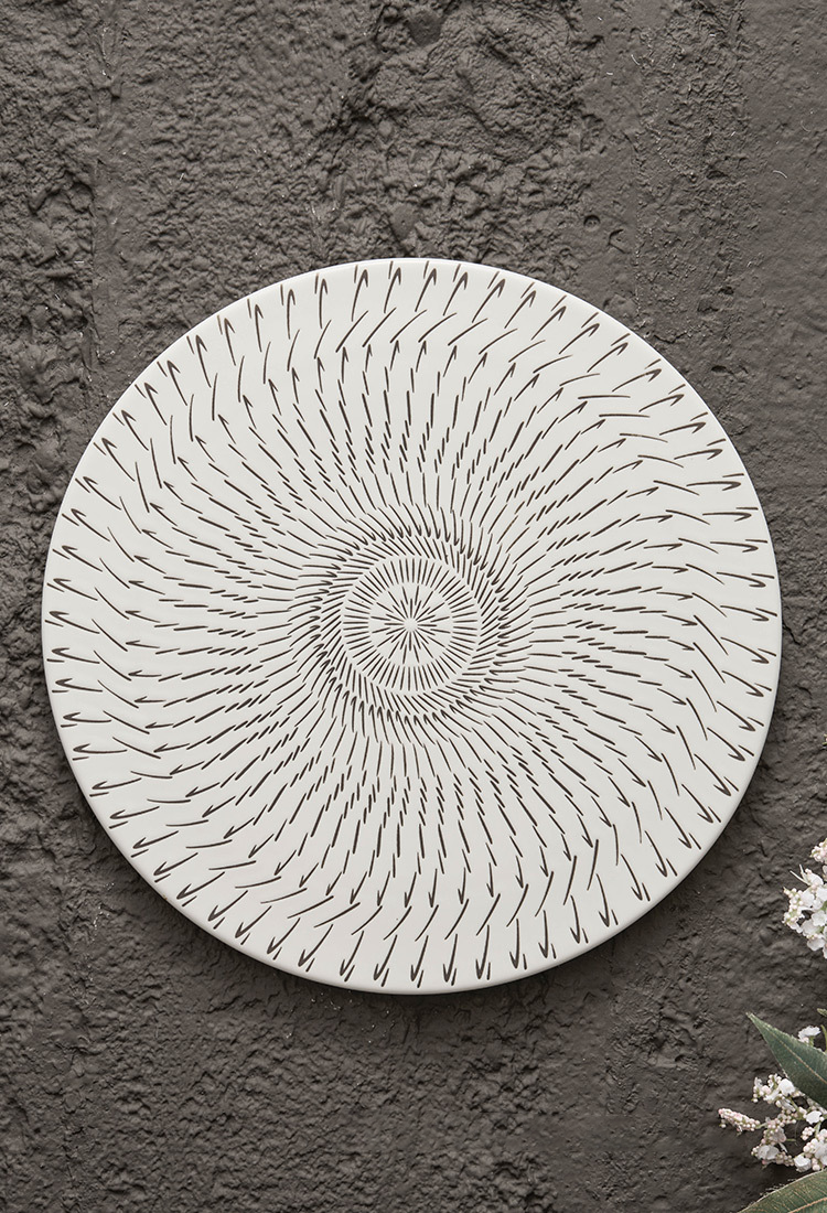 Round ceramic wall art with concentric circle pattern on a textured gray wall.