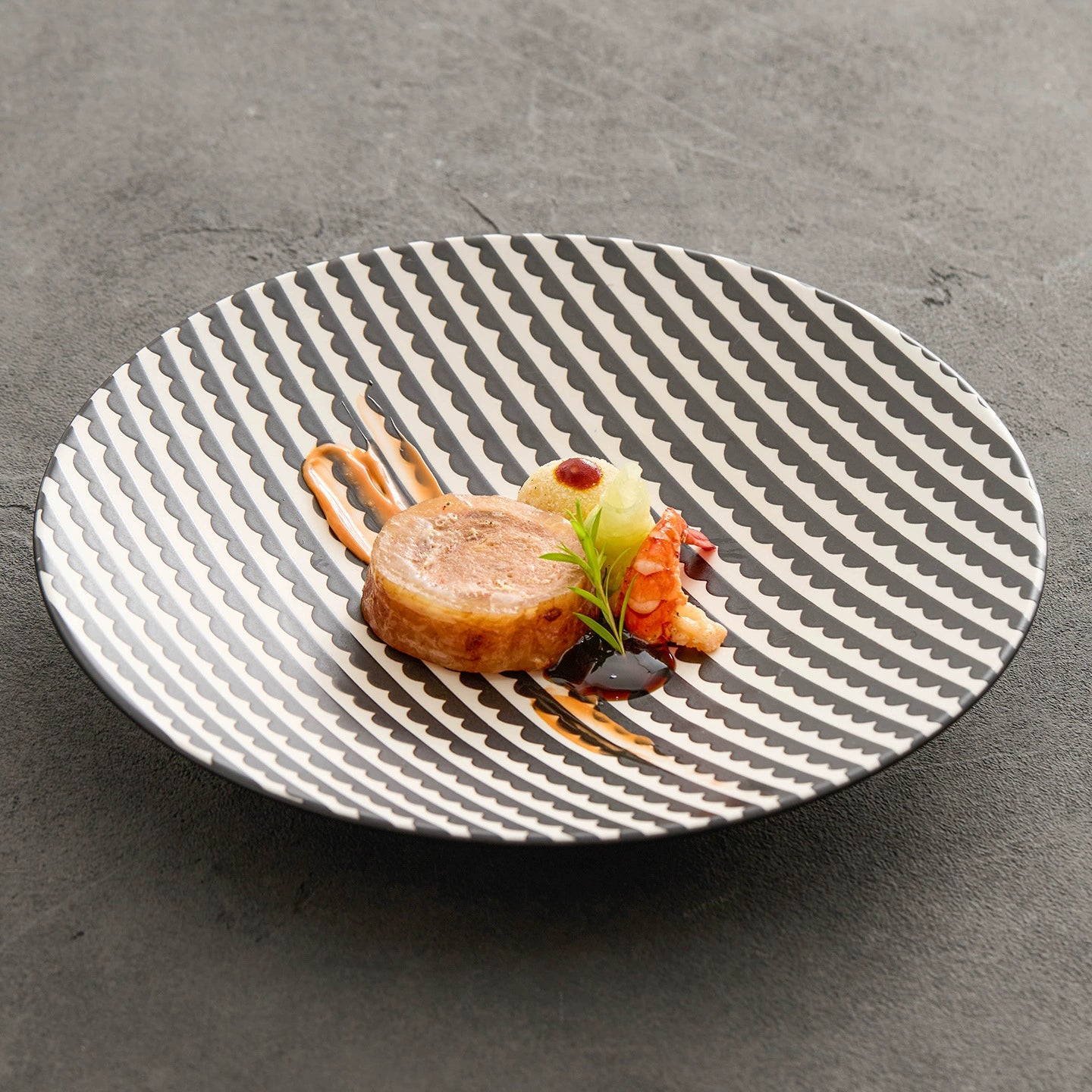 Elegant dish with food on a black and white patterned plate against a gray background