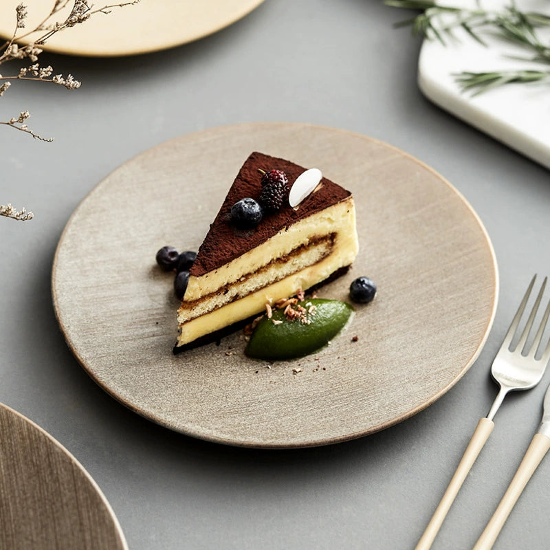 Slice of layered cake on a textured plate with berries and a leaf, on a gray surface.