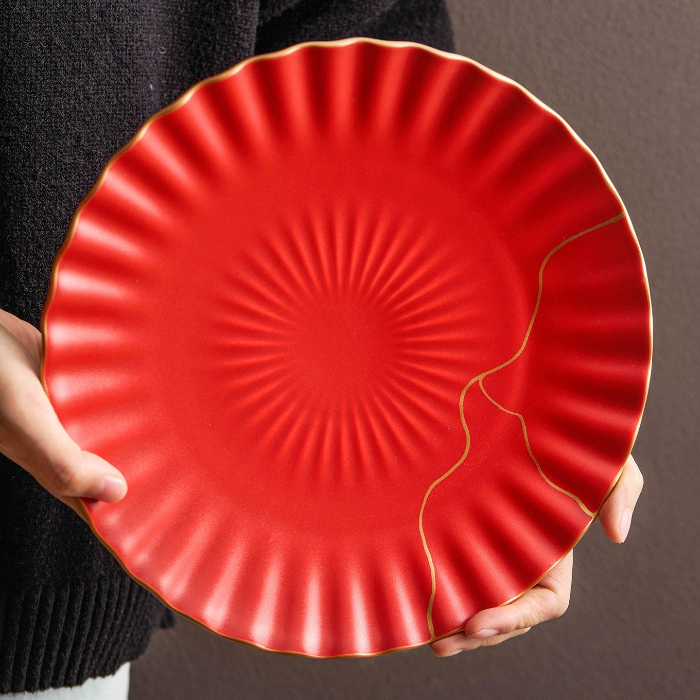 Red ceramic plate with gold accents held by a person against a neutral background