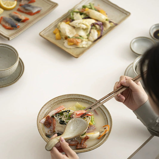 Natural glazed ceramic plates, bowls, cups, and chopsticks set on white table

