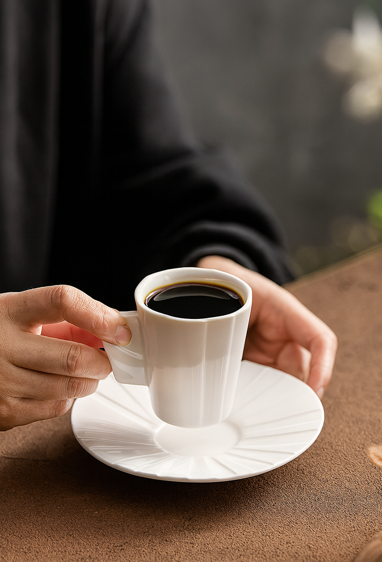 Origami-style coffee cup with saucer in minimalist table setting.