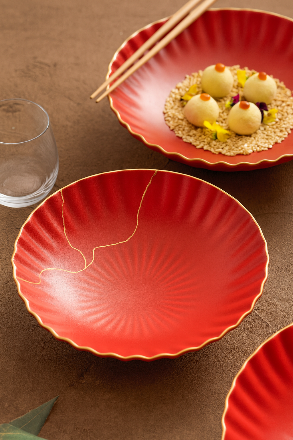 Red ceramic plate with a decorative crack on a brown surface, accompanied by a glass and chopsticks.