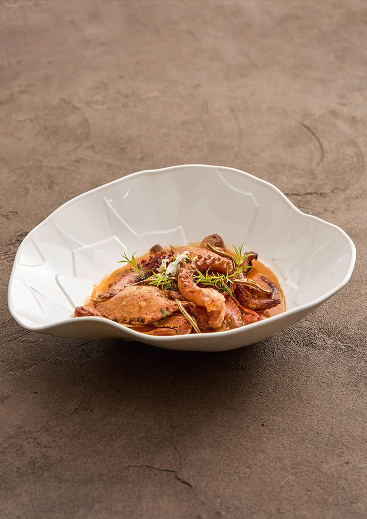 Seafood curry presented in a wide-rimmed sculptural ceramic basin.