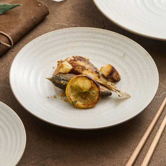 Shallow ceramic plate with grilled fish and lemon garnish

