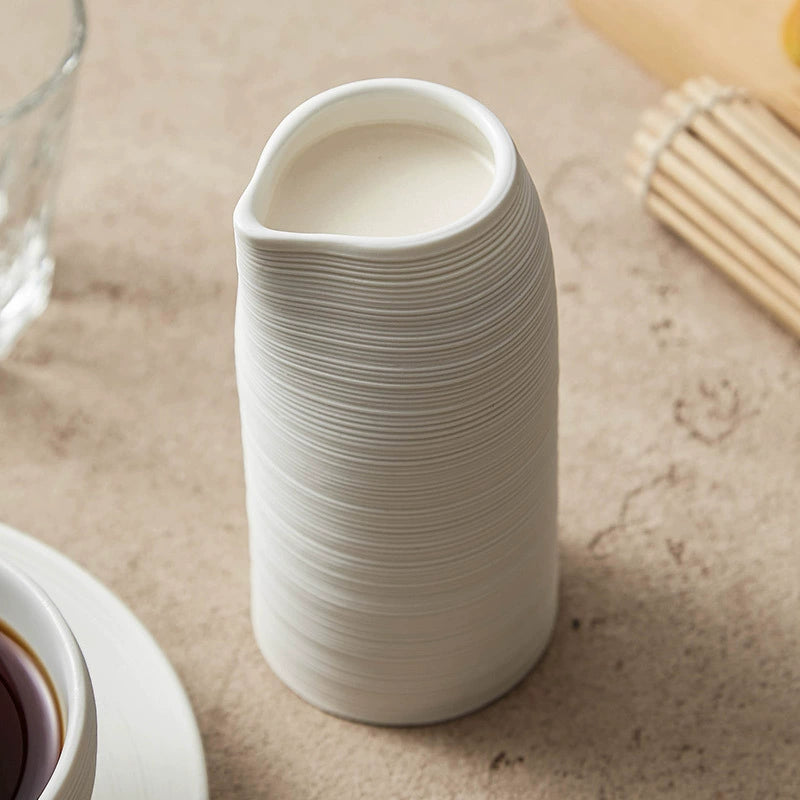 White ceramic vase on a textured surface with a glass and wooden items in the background