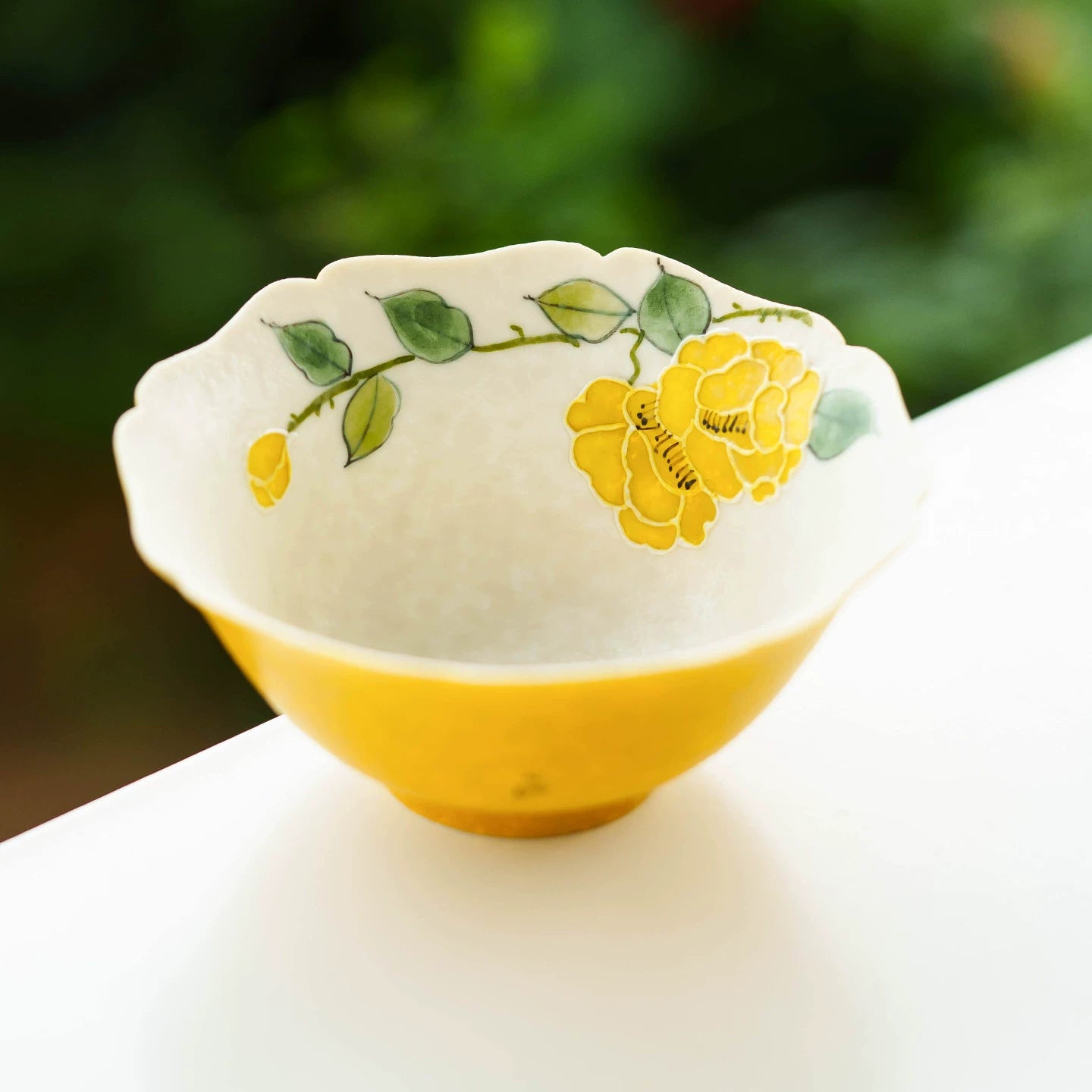 Top-down view of a 70ml porcelain cup showing hand-painted yellow camellia and green leaves.