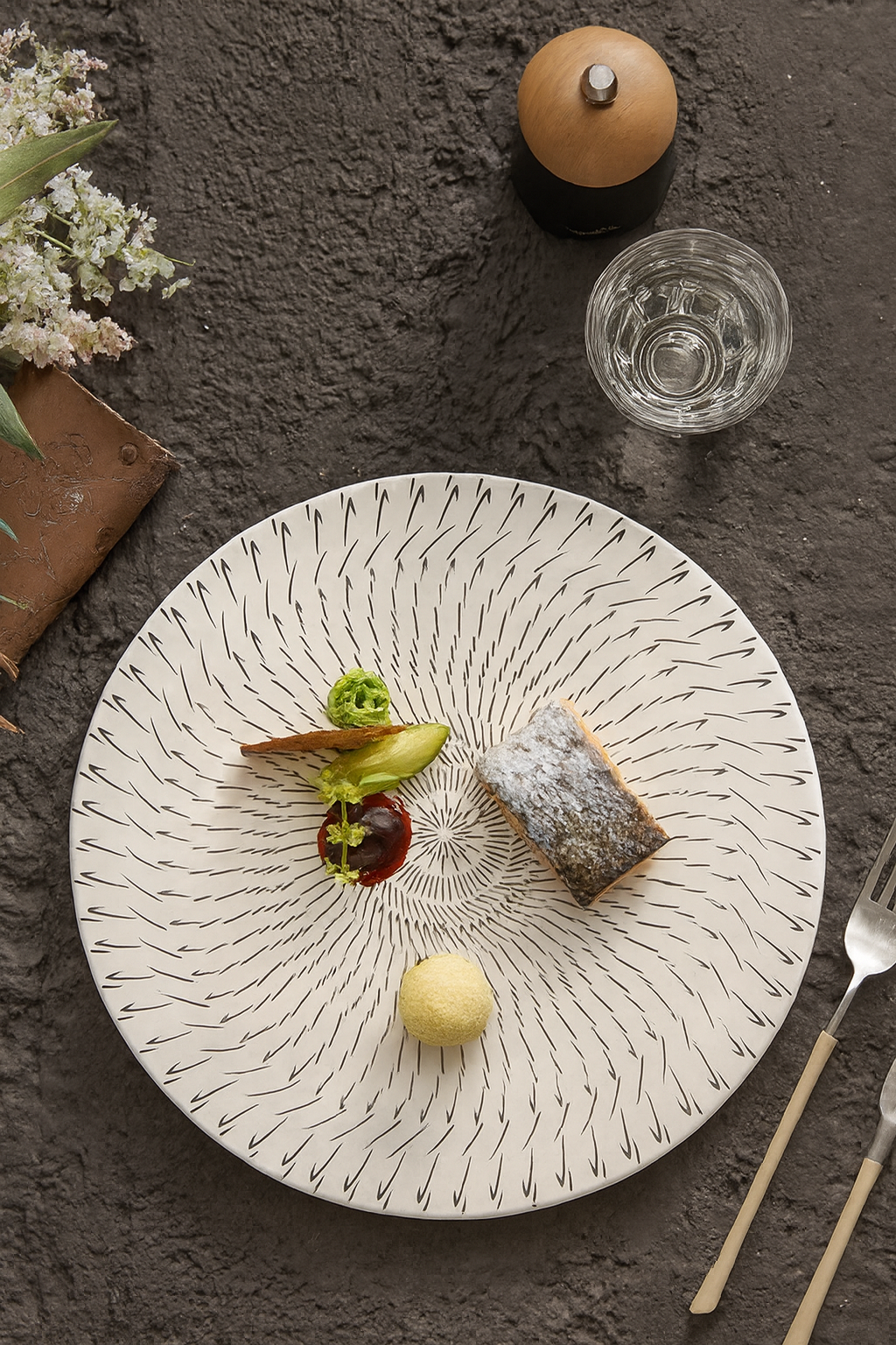 Decorative plate with food on a textured surface with a glass of water and utensils.