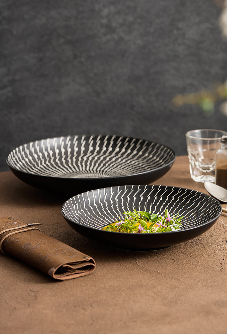 Black textured plates with a salad on a brown surface, against a dark background