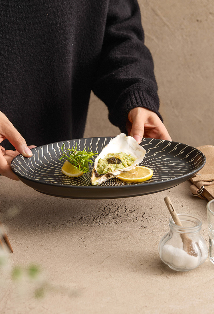 Person holding a black decorative plate with food on a beige surface