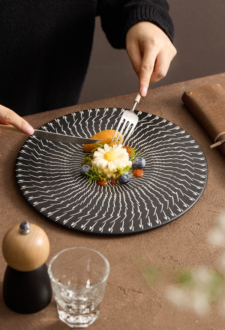 Person using a fork to eat a dish on a decorative black plate with a textured pattern.