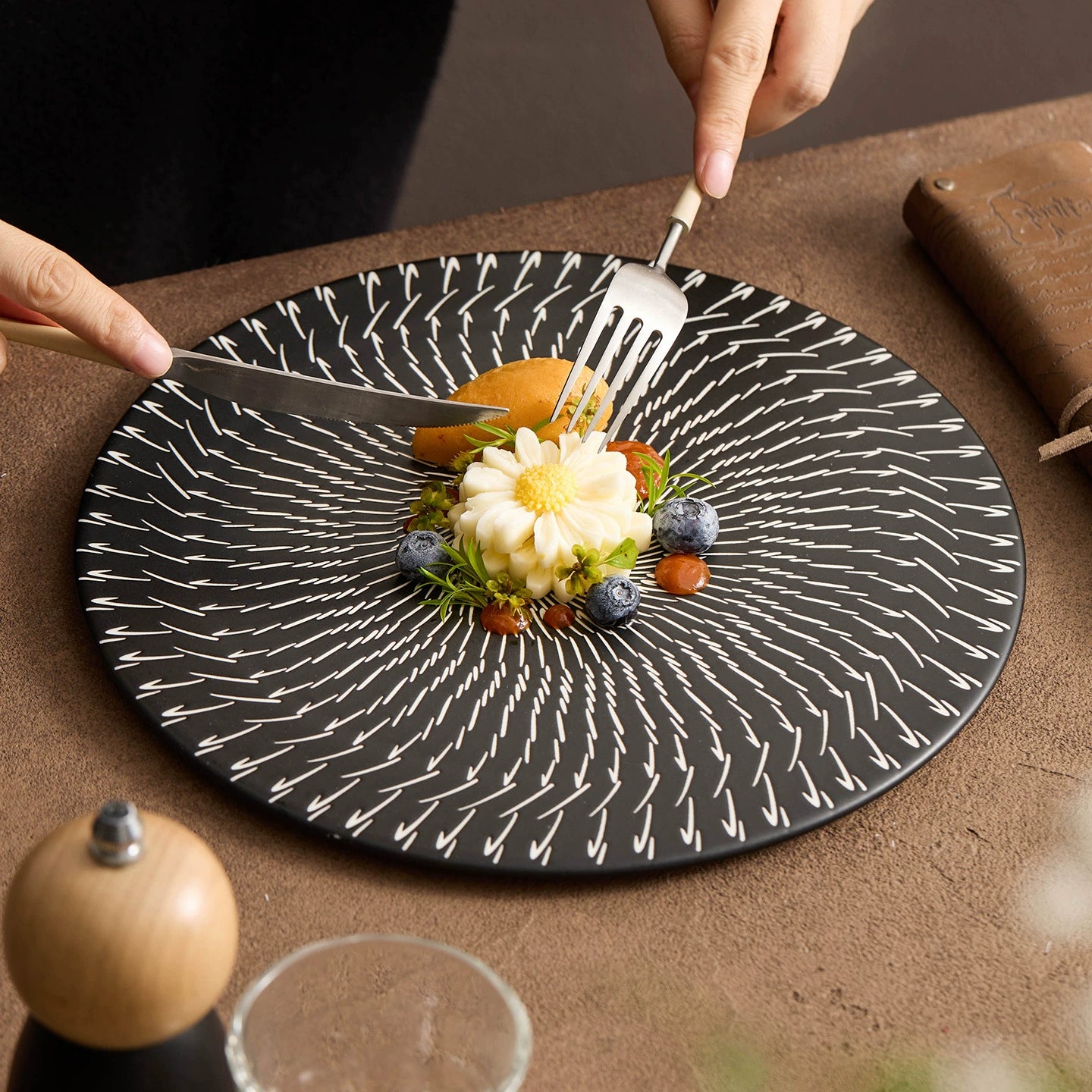 Dessert on a black patterned plate with a fork and knife, on a brown surface.