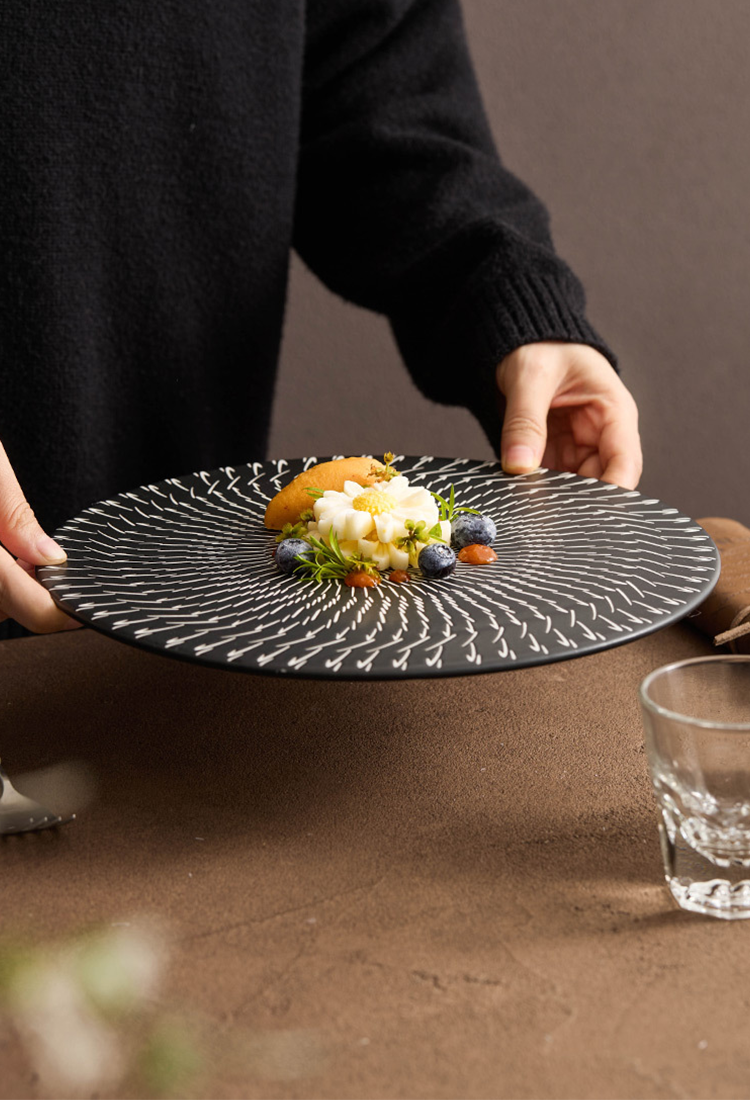 Person holding a black decorative plate with a dish on a brown surface