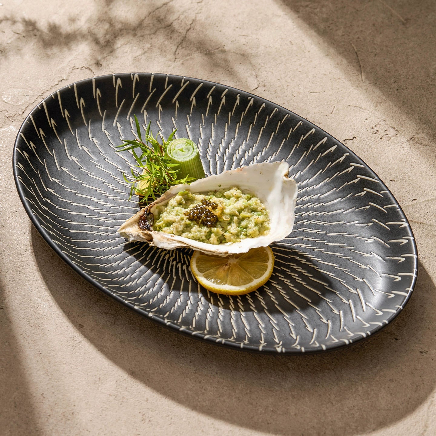 Oyster with lemon wedge on a decorative black plate on a textured surface