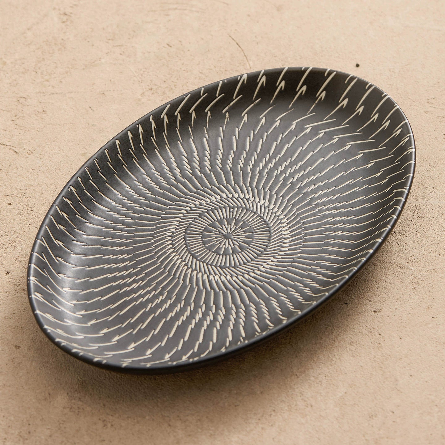 Black ceramic plate with white spiral design on a beige background